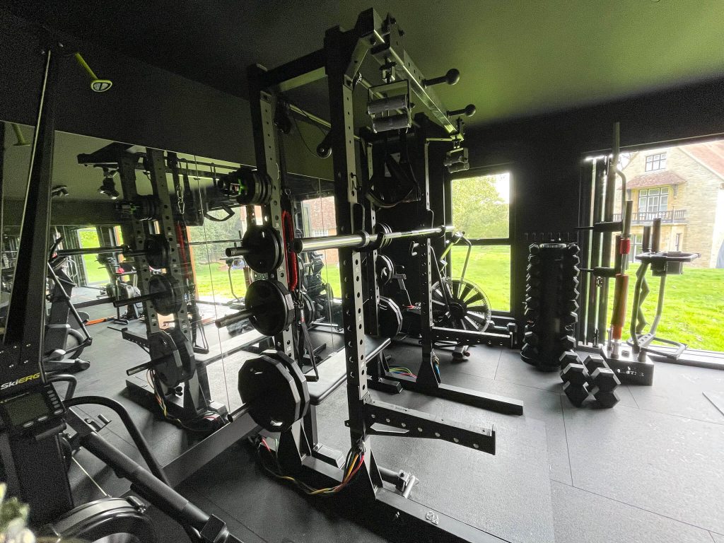 Inside garden gym with matting covering floor, large mirror and multi use equipment