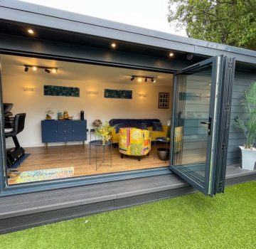 Large bifold doors open looking into garden room with yellow chairs
